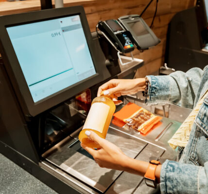 A girl customer scanns and pays for bottle of juice from a supermarket in an automated self-service checkout terminal